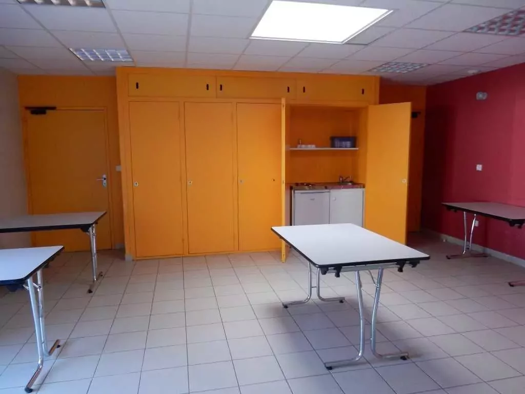 Intérieur de la Salle Barbara à Bourgneuf-en-Mauges, avec tables disposées dans la pièce et kitchenette