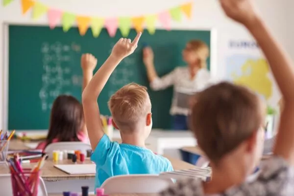 Des enfants en classe lèvent le doigt