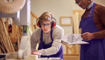Apprenti menuisier avec son tuteur utilisant une scie