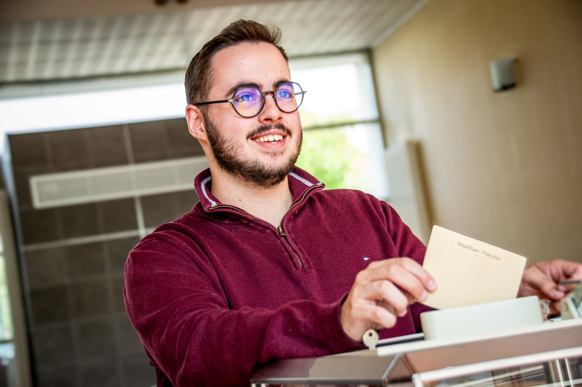 personne souriante qui met son bulletin de vote dans l'urne