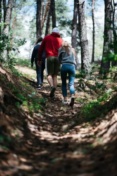 femme en veste marron marchant sur un sentier entre les arbres en plein jour
