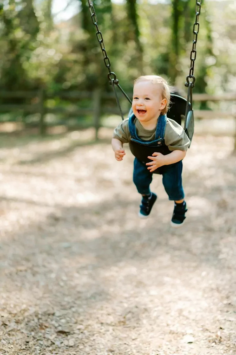 A happy baby boy swinging on a playground swing